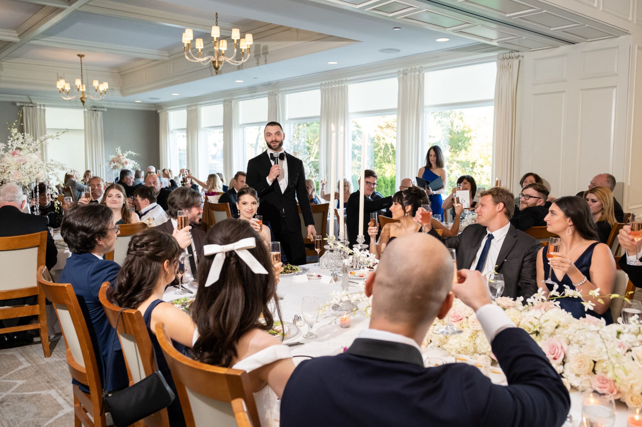 Wedding guest giving a speech while guests listen and raise their glasses at the reception