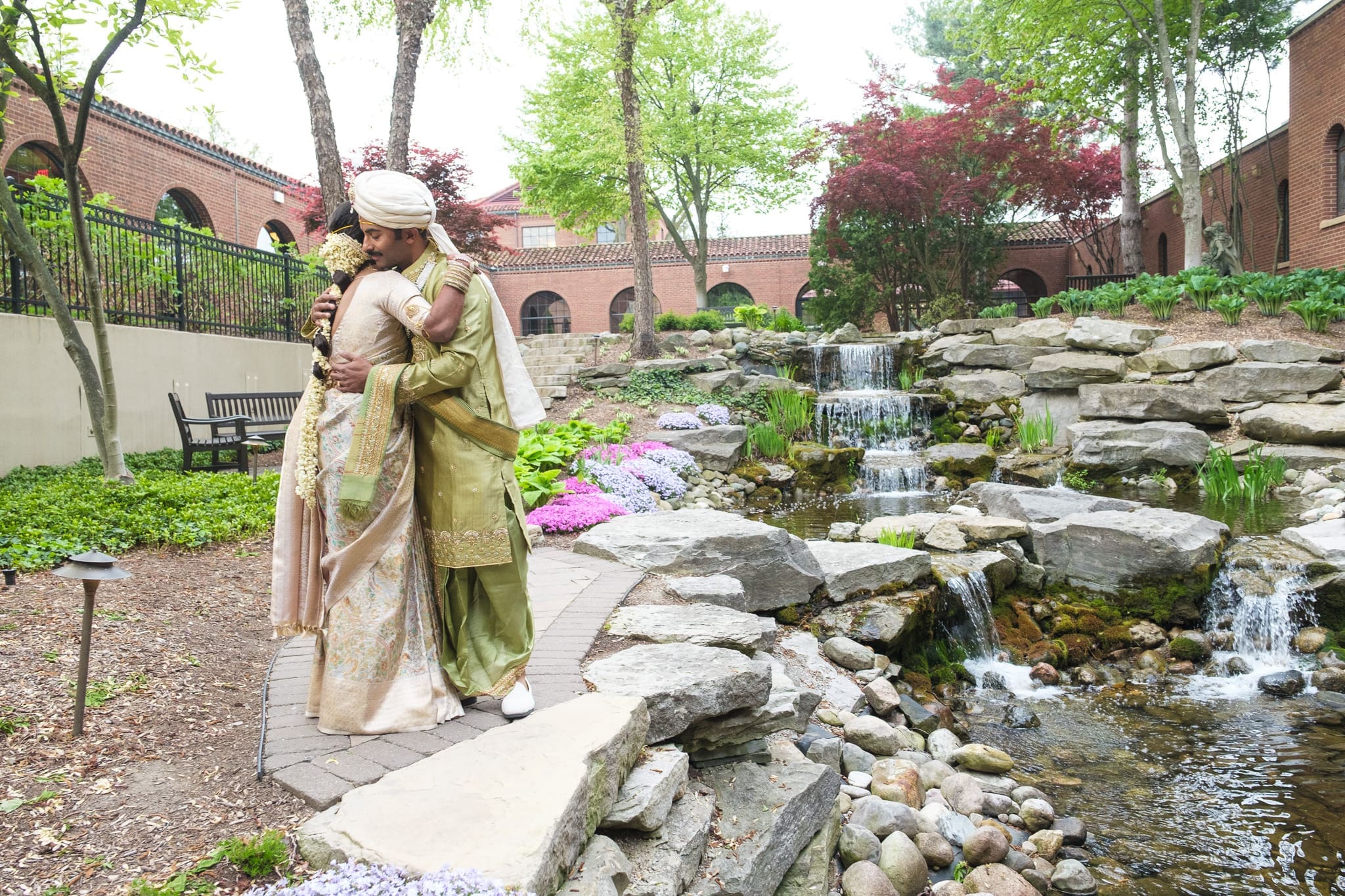 South Asian bride and groom posing beside a garden stream during their wedding portrait session.