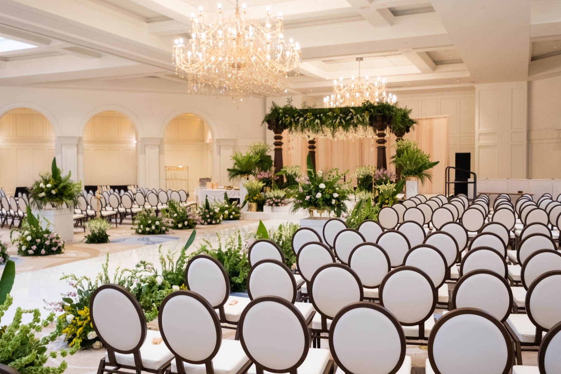Wedding ceremony seating and floral mandap inside Monarch Ballroom at Saint John's Resort, featuring elegant chandeliers, luxury décor, and a spacious ballroom setting.
