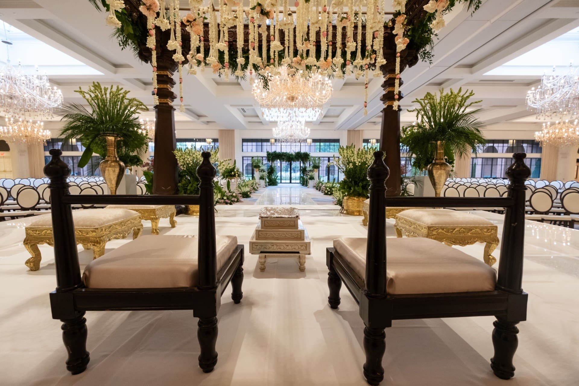 Traditional Indian wedding mandap inside Monarch Ballroom at Saint John's Resort featuring ornate seating, floral garlands, elegant décor, and crystal chandeliers.