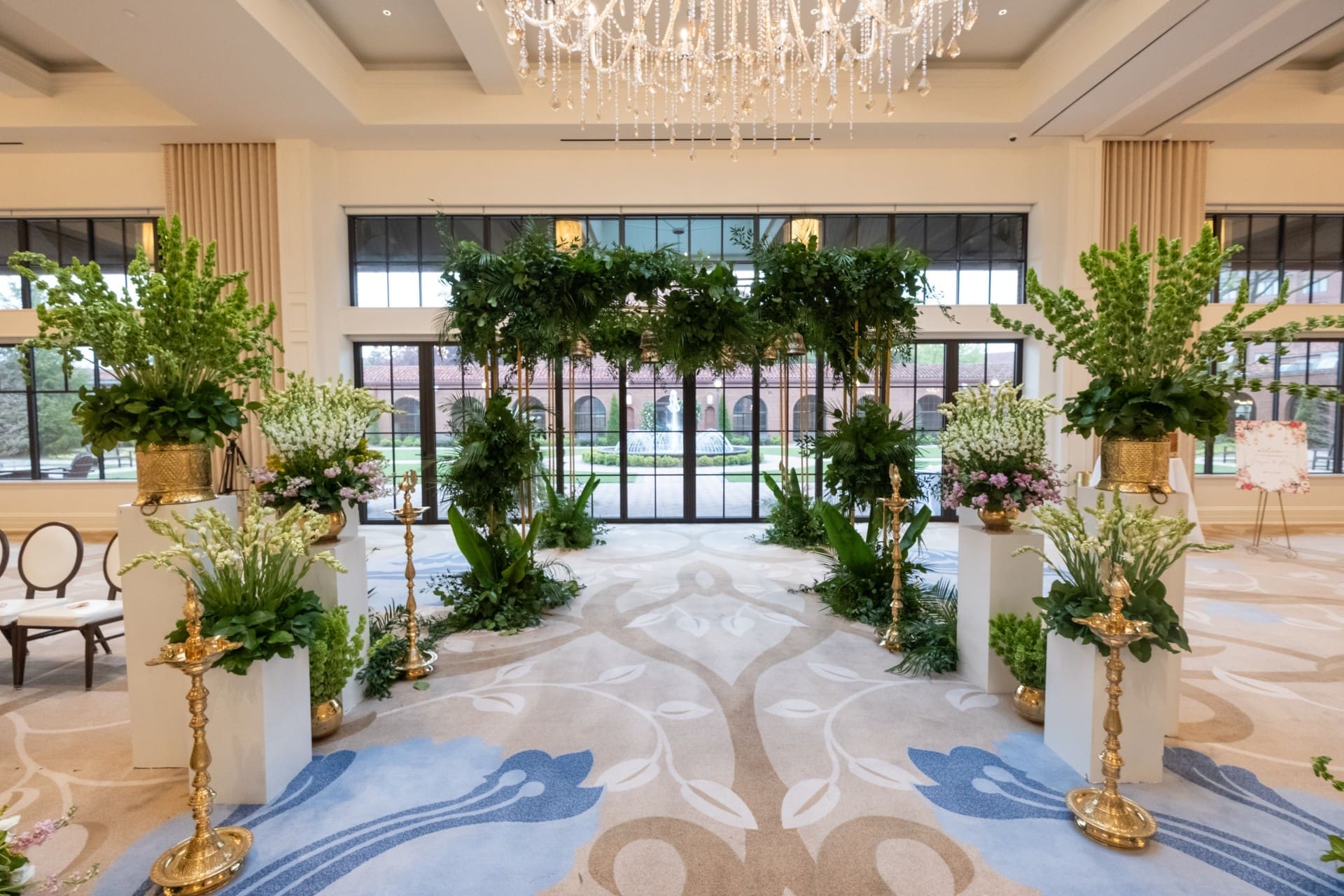 Elegant wedding ceremony setup inside Monarch Ballroom at Saint John's Resort featuring lush greenery, floral arrangements, crystal chandeliers, and floor-to-ceiling windows.