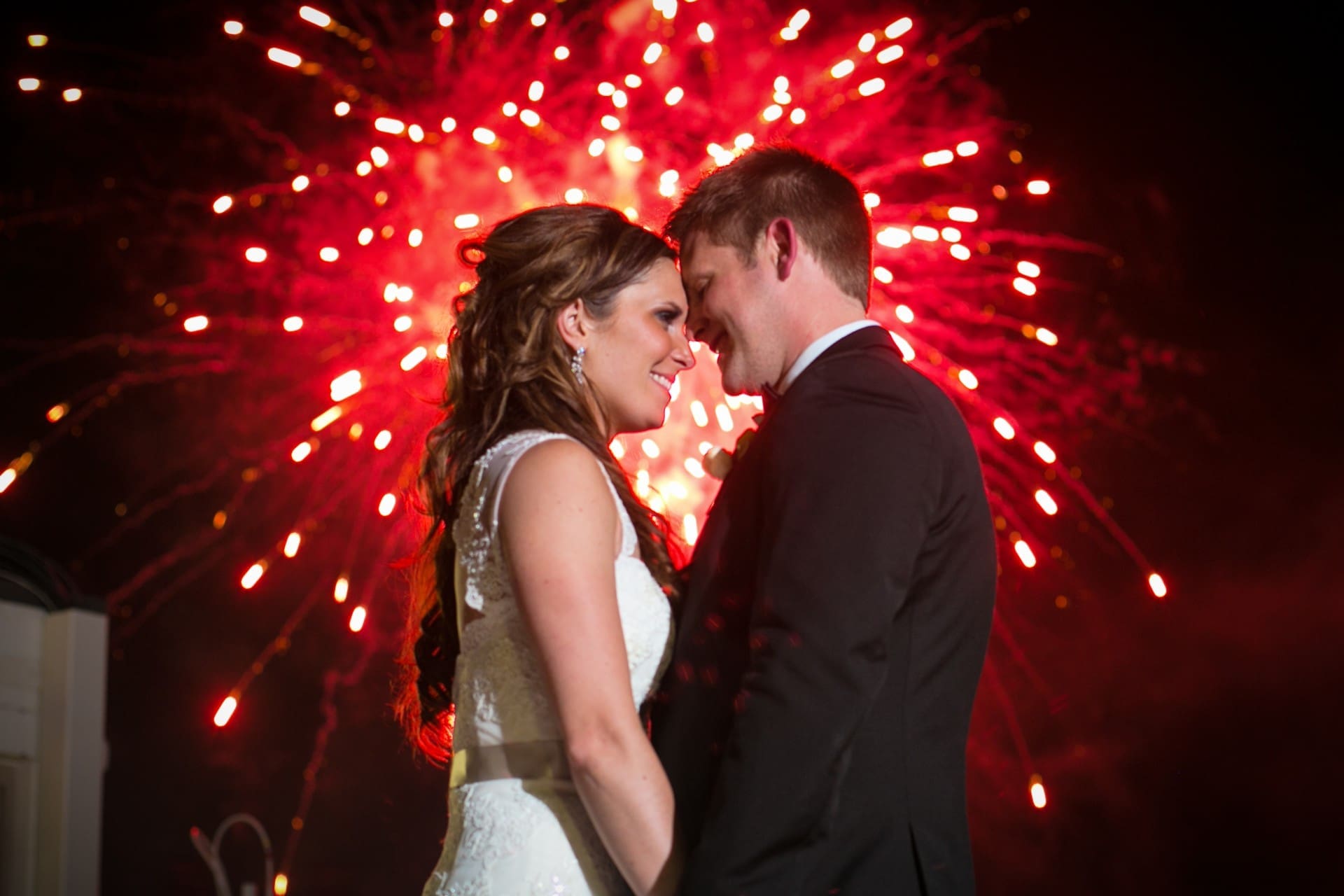 Bride and groom sharing a romantic moment during their Detroit wedding reception with fireworks in the background.