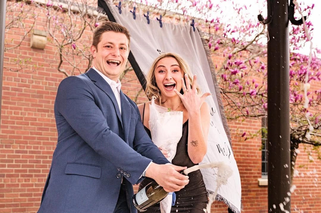 Recently engaged couple celebrating with champagne during a Detroit proposal photo session.
