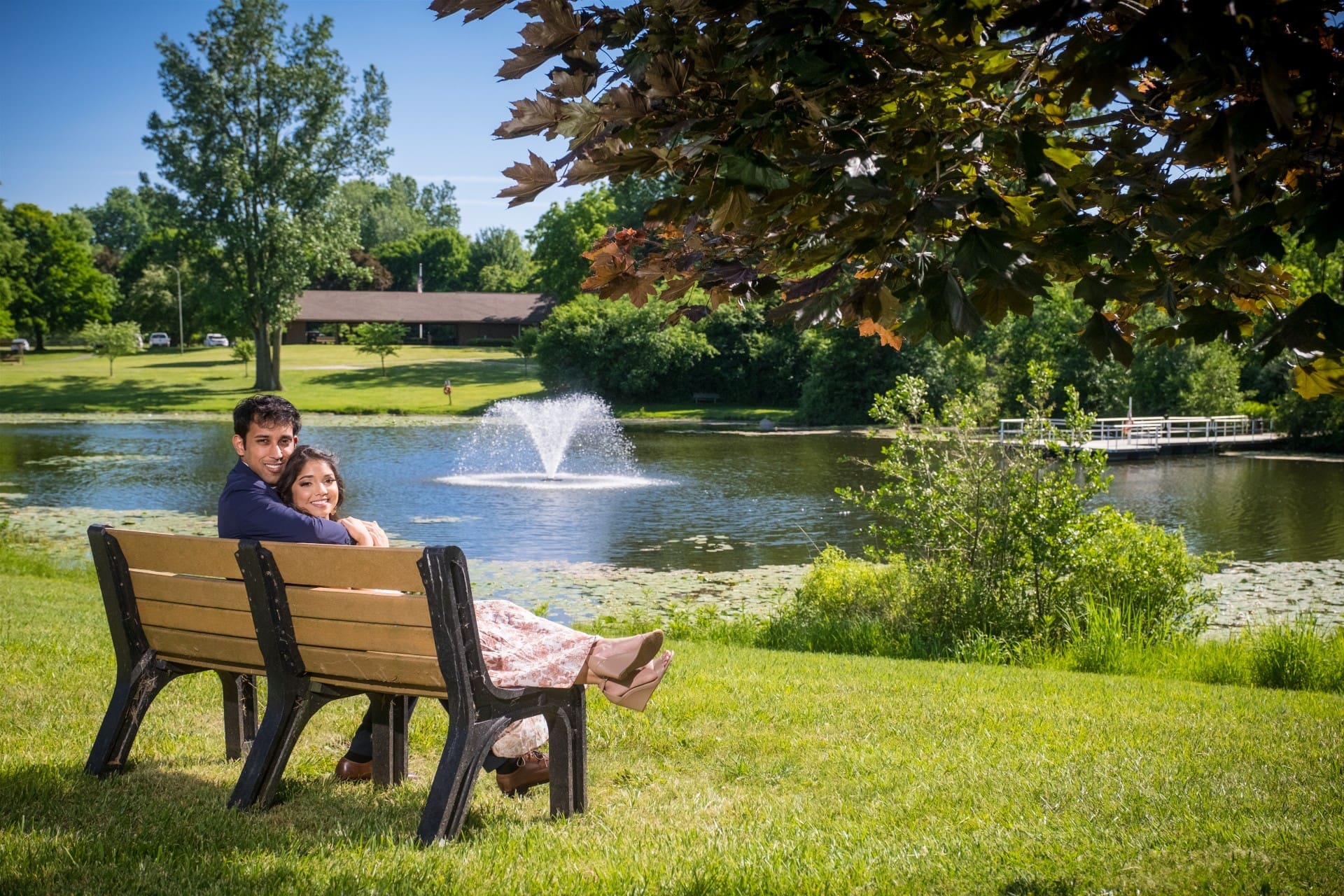 Couple relaxing on a park bench during a romantic engagement photo shoot.