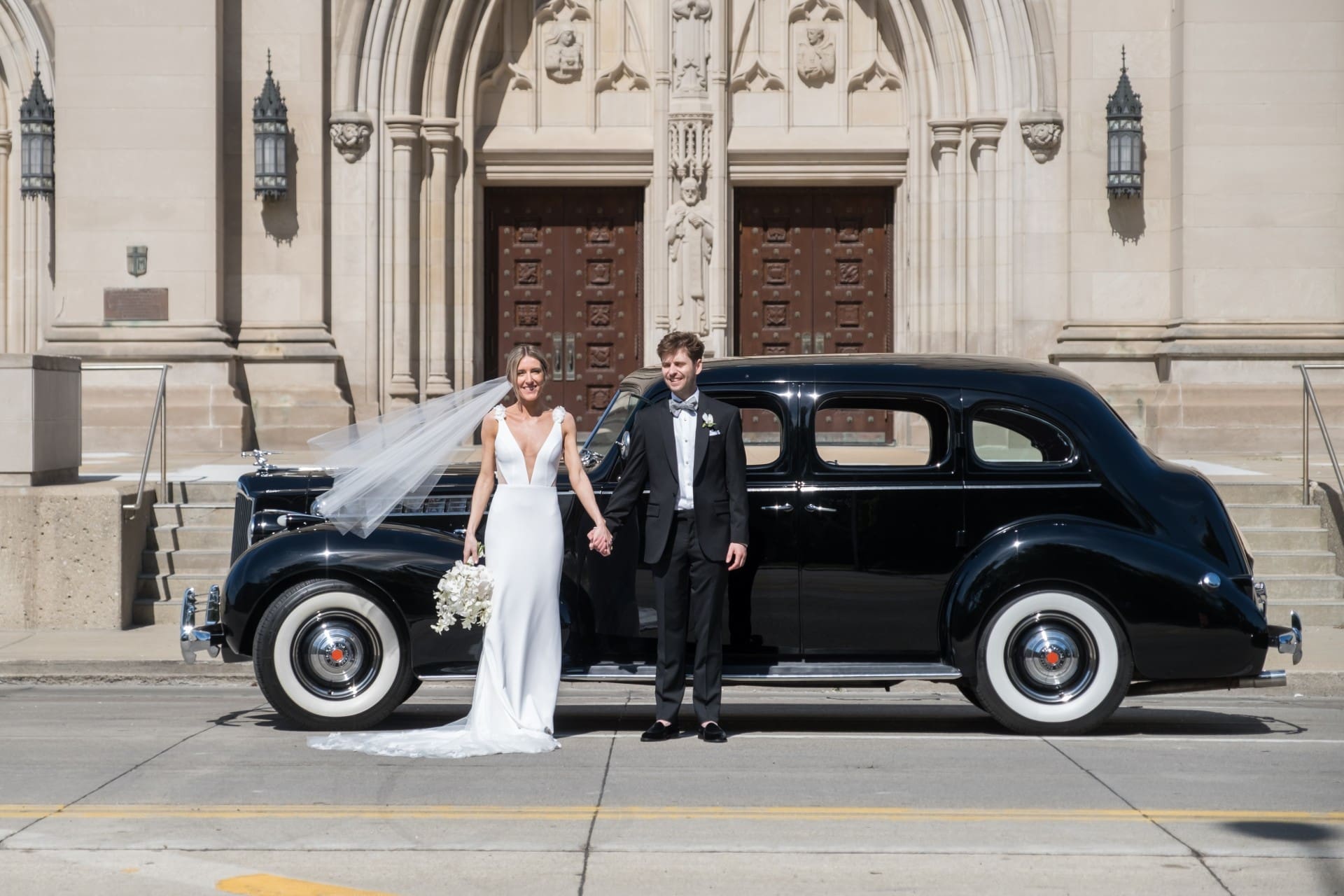 Bride and groom posing beside a vintage car on their Detroit wedding day.
