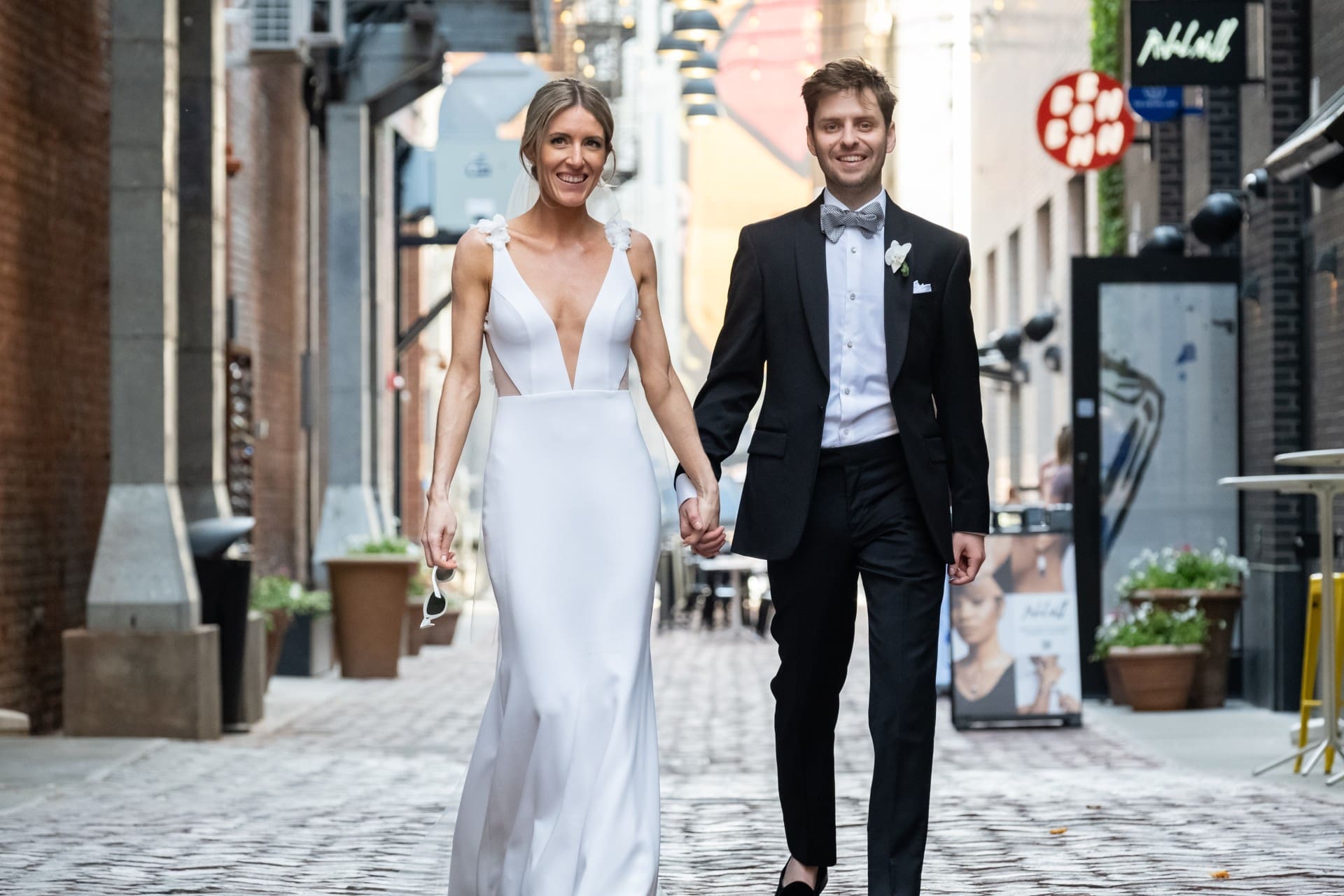 Bride and groom walking hand in hand through a charming city street.