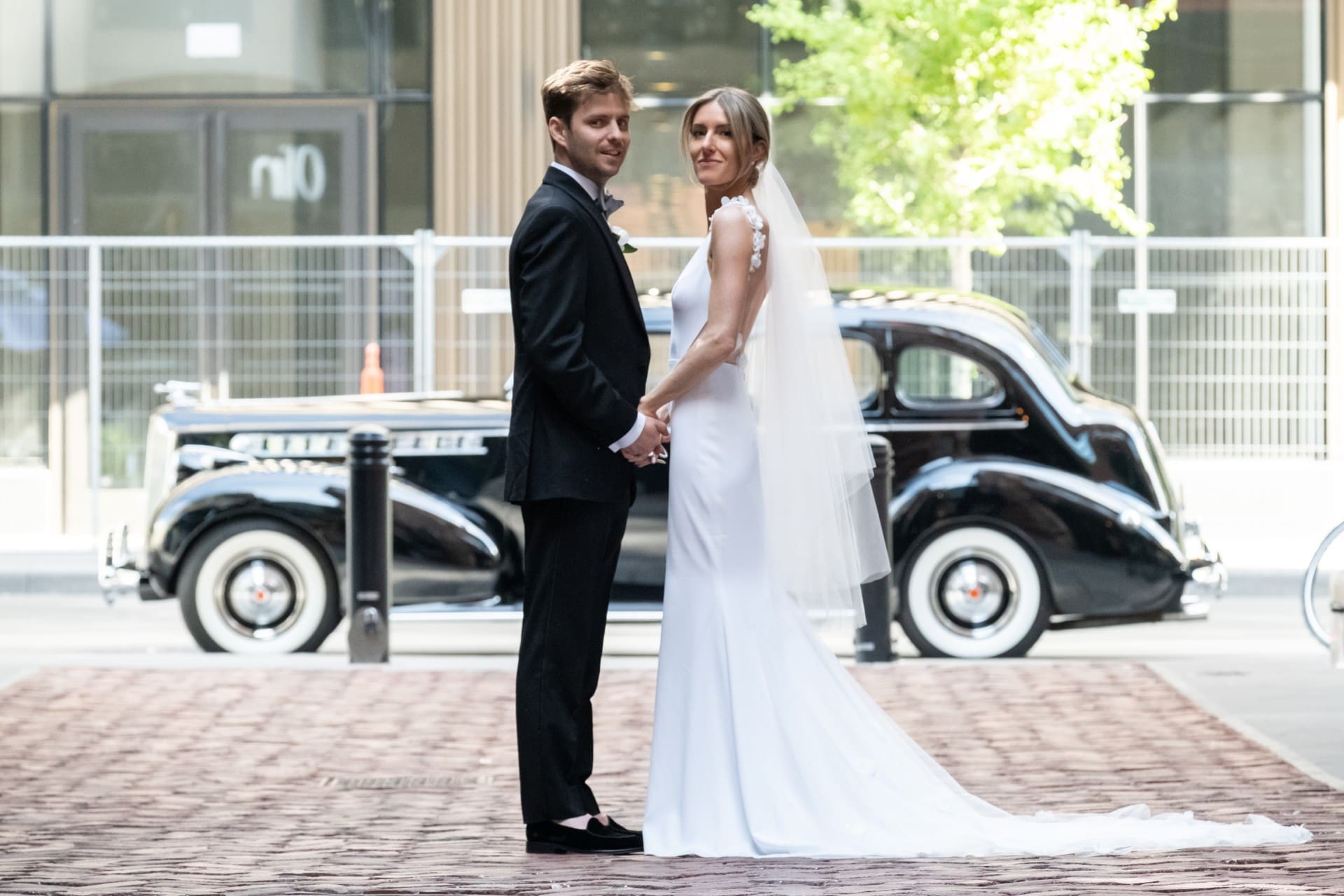 Bride and groom holding hands beside a classic vintage car.