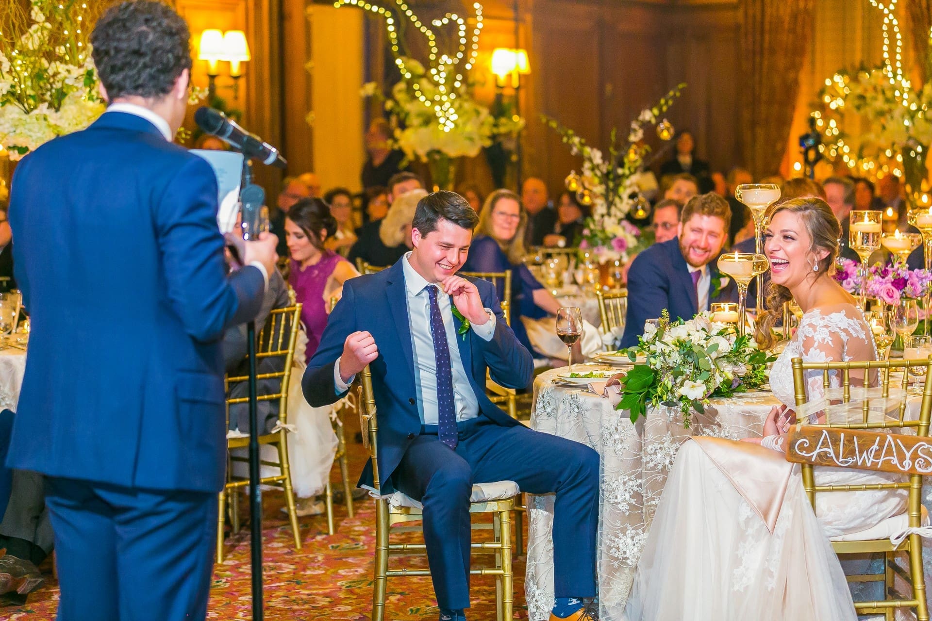 Wedding guest giving a speech as the groom laughs and the bride smiles at the reception