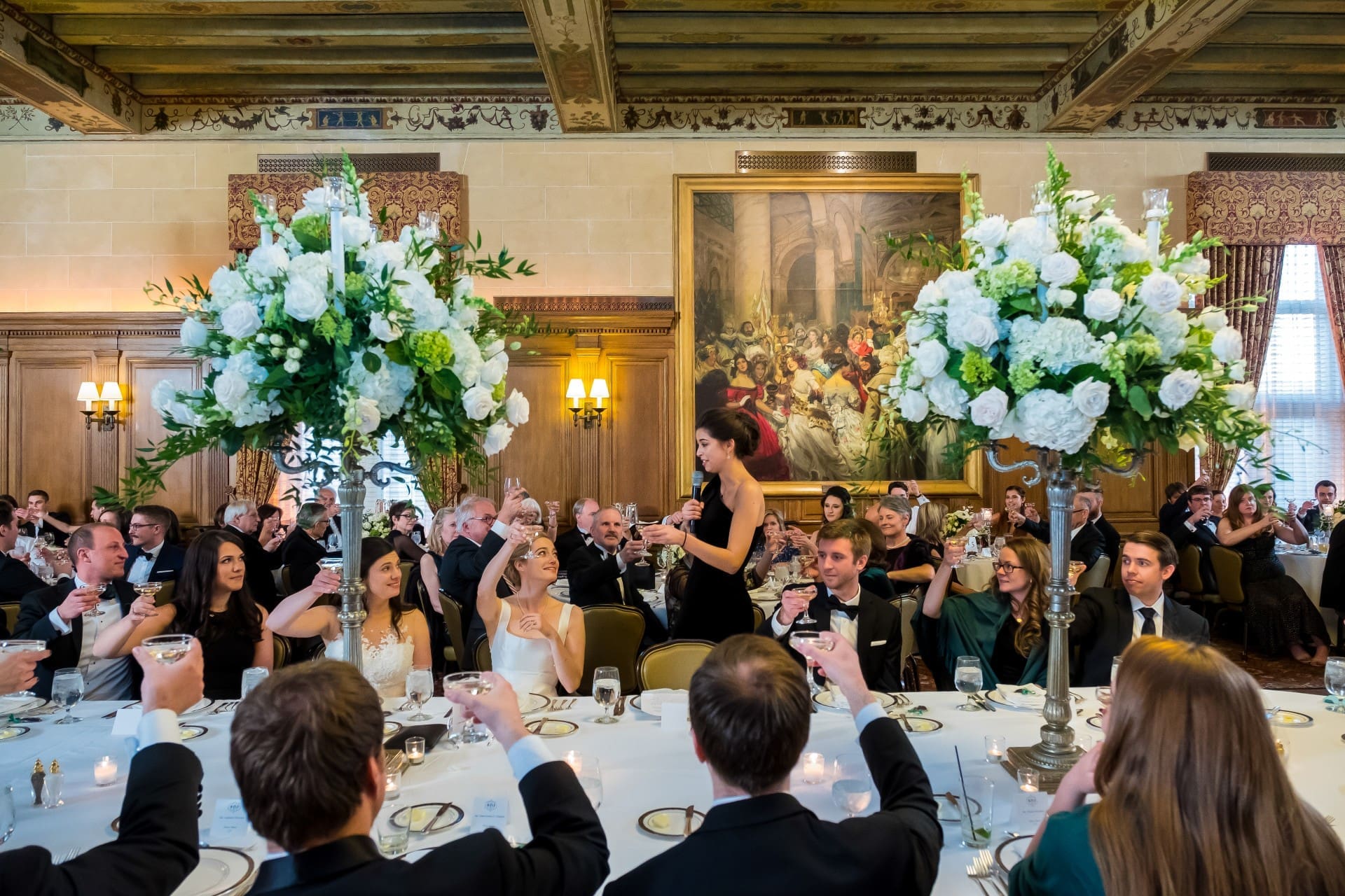 Guests raising champagne glasses together while seated at decorated tables