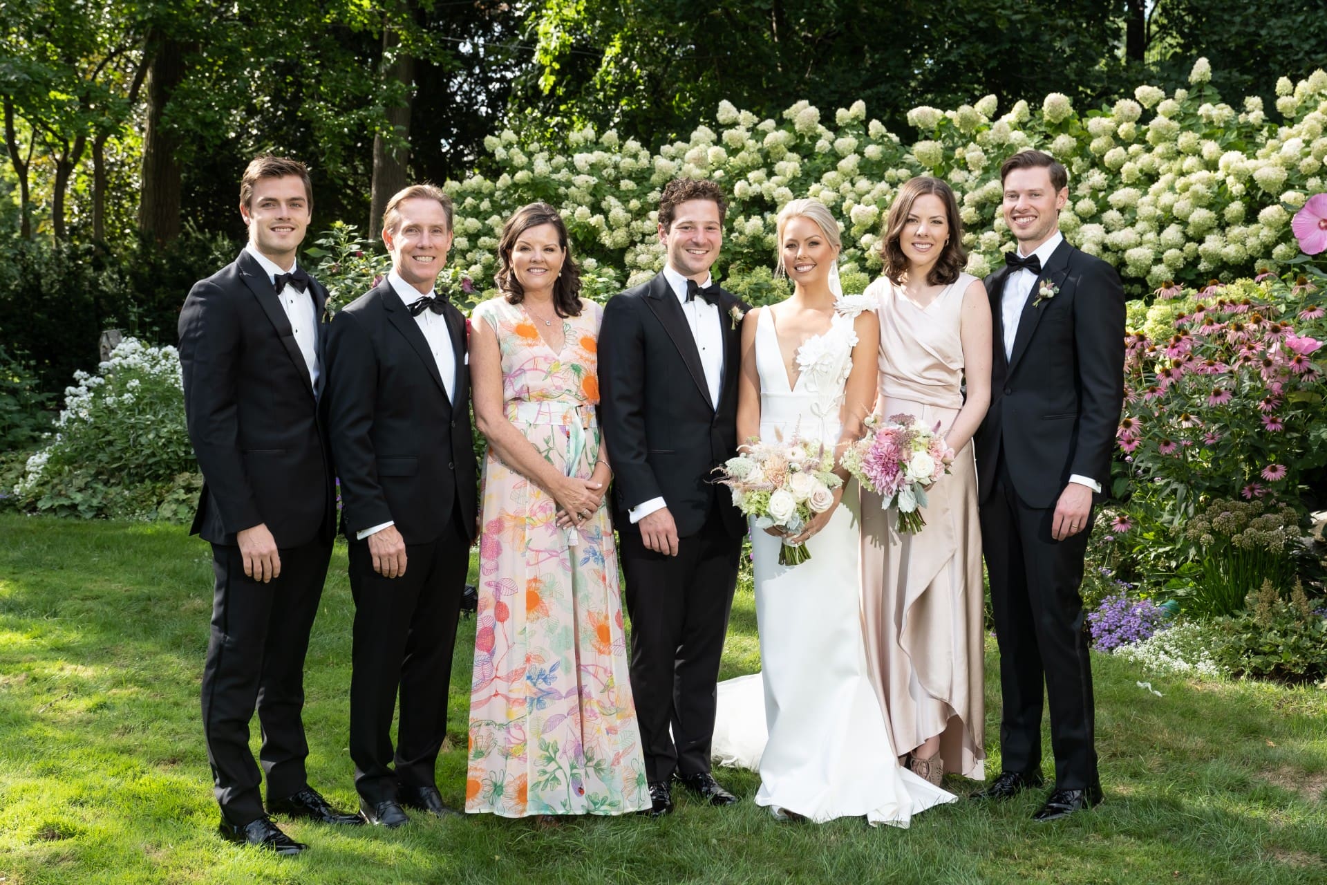 Bloomfield Hills wedding couple posing with family members in a garden surrounded by blooming hydrangeas