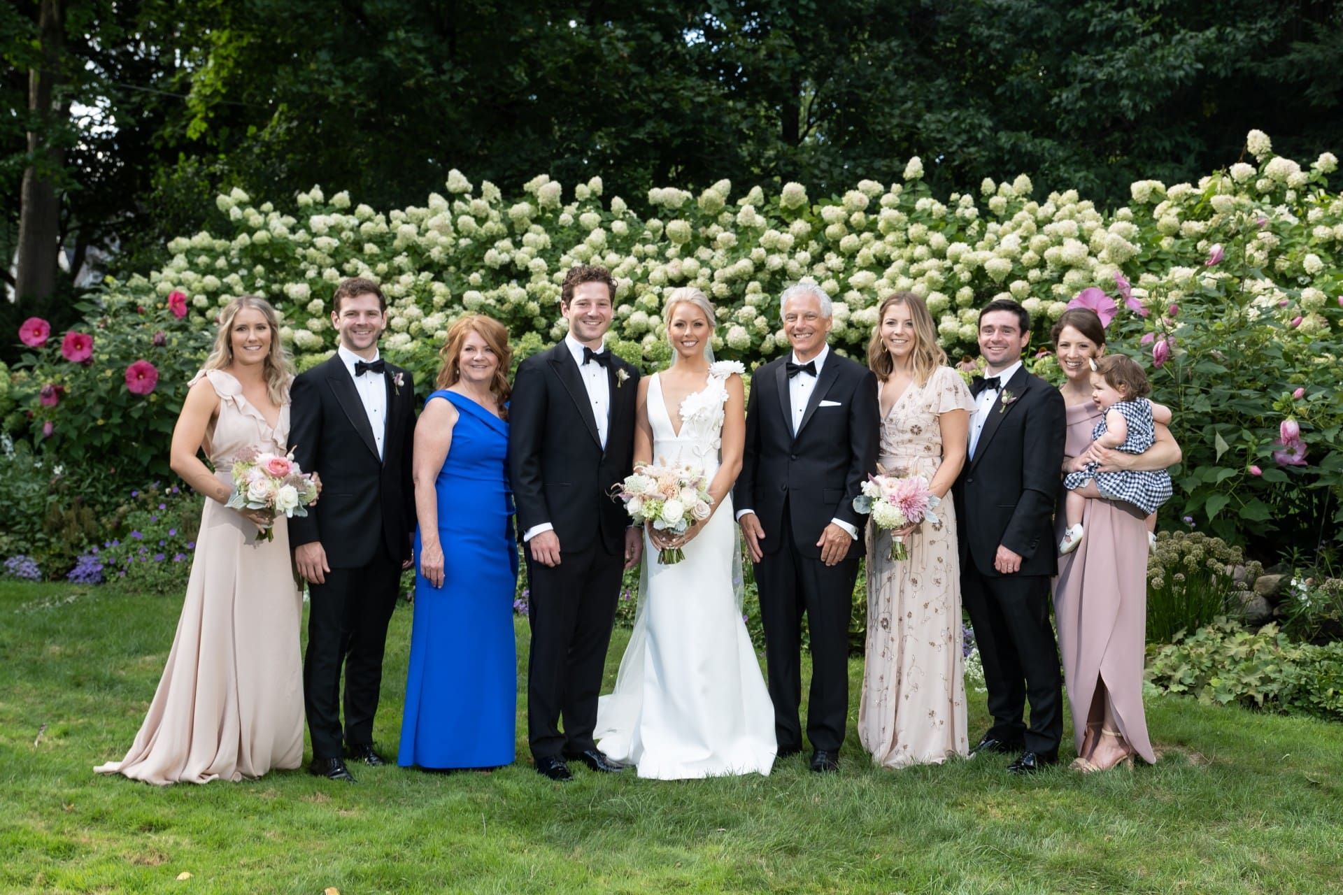 Bride and groom posing with family members in a garden surrounded by blooming hydrangeas