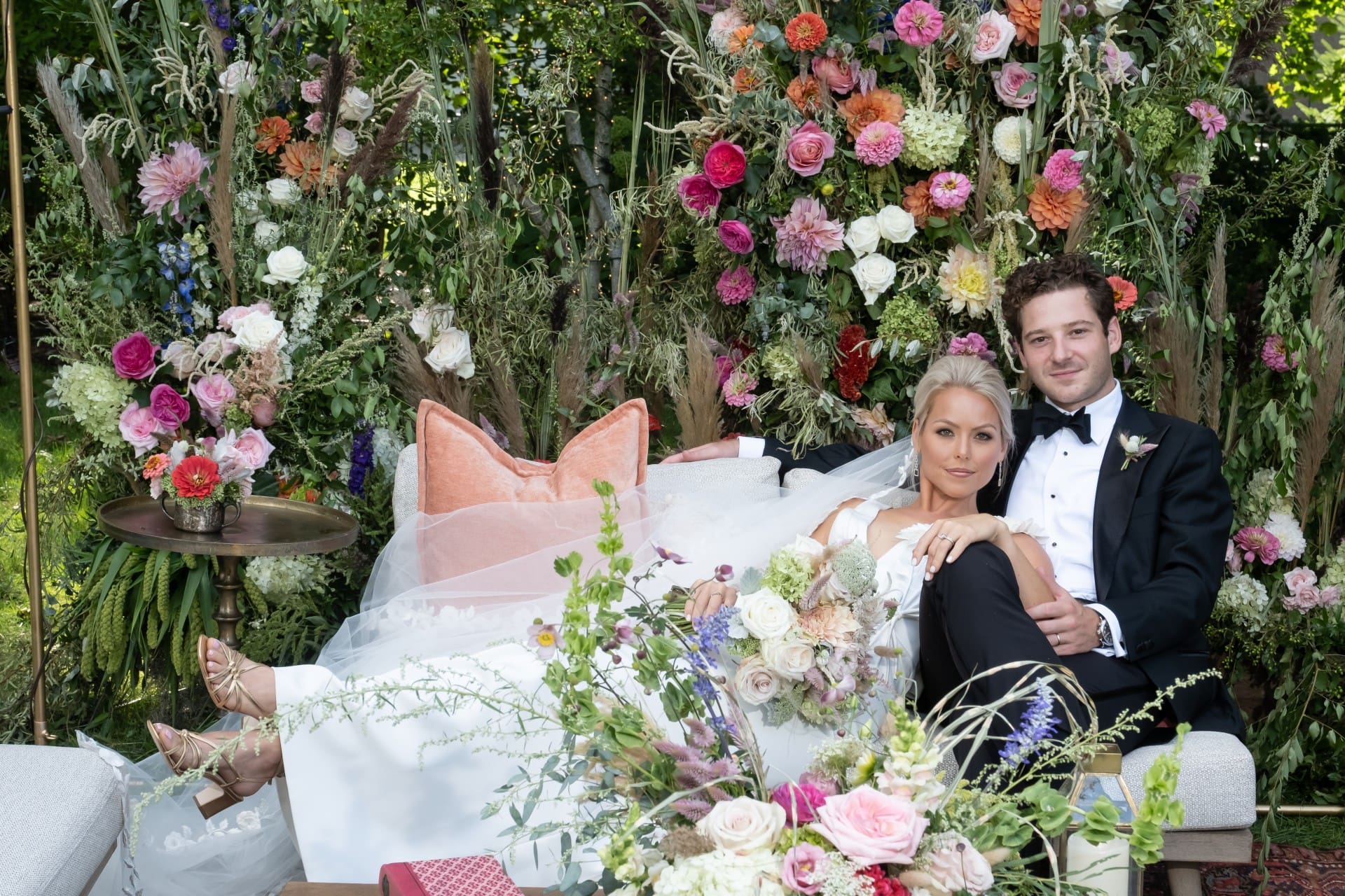 Bride and groom relaxing together surrounded by colorful floral arrangements and lush greenery