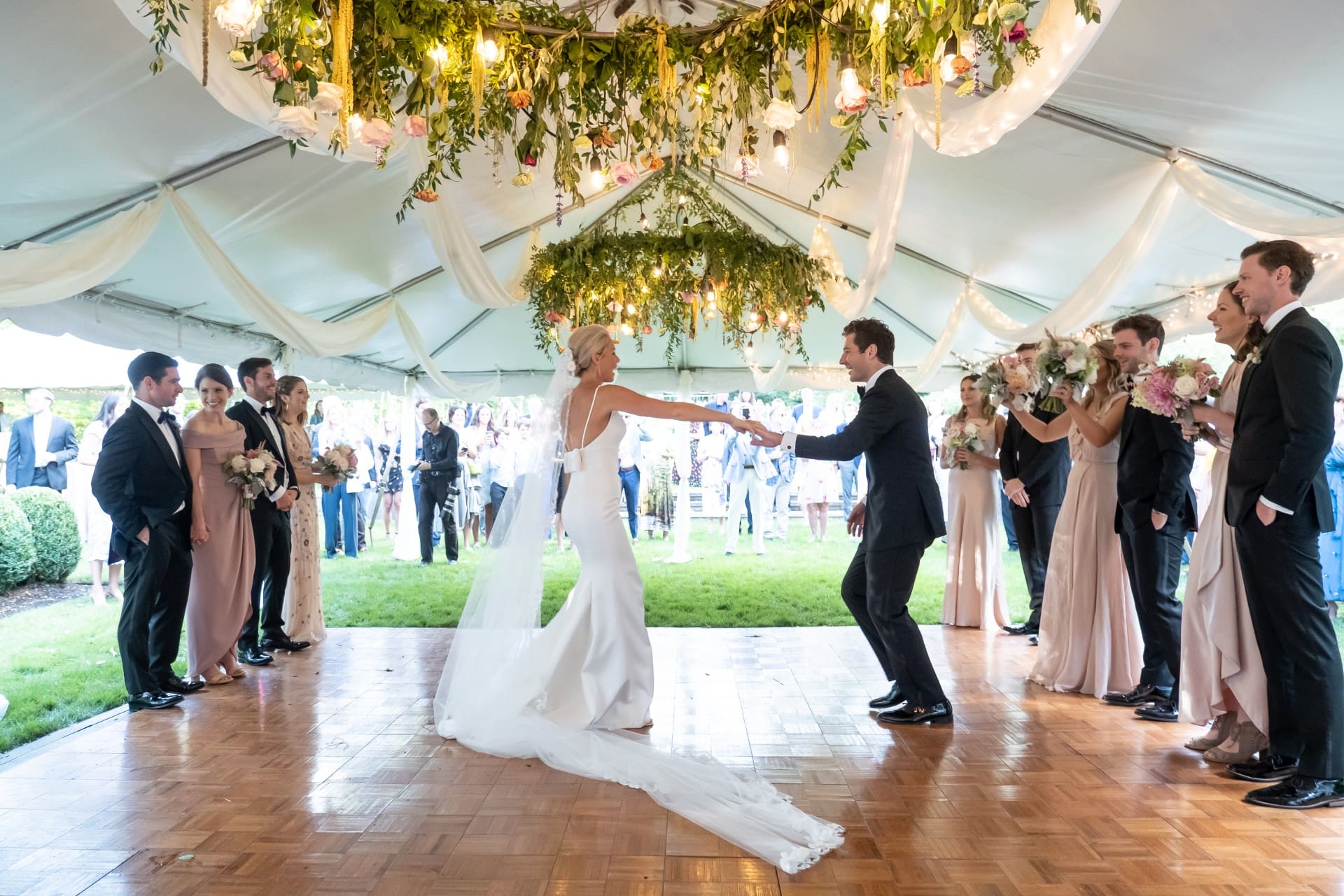 Bride and groom dancing together with their wedding party beneath a floral reception canopy
