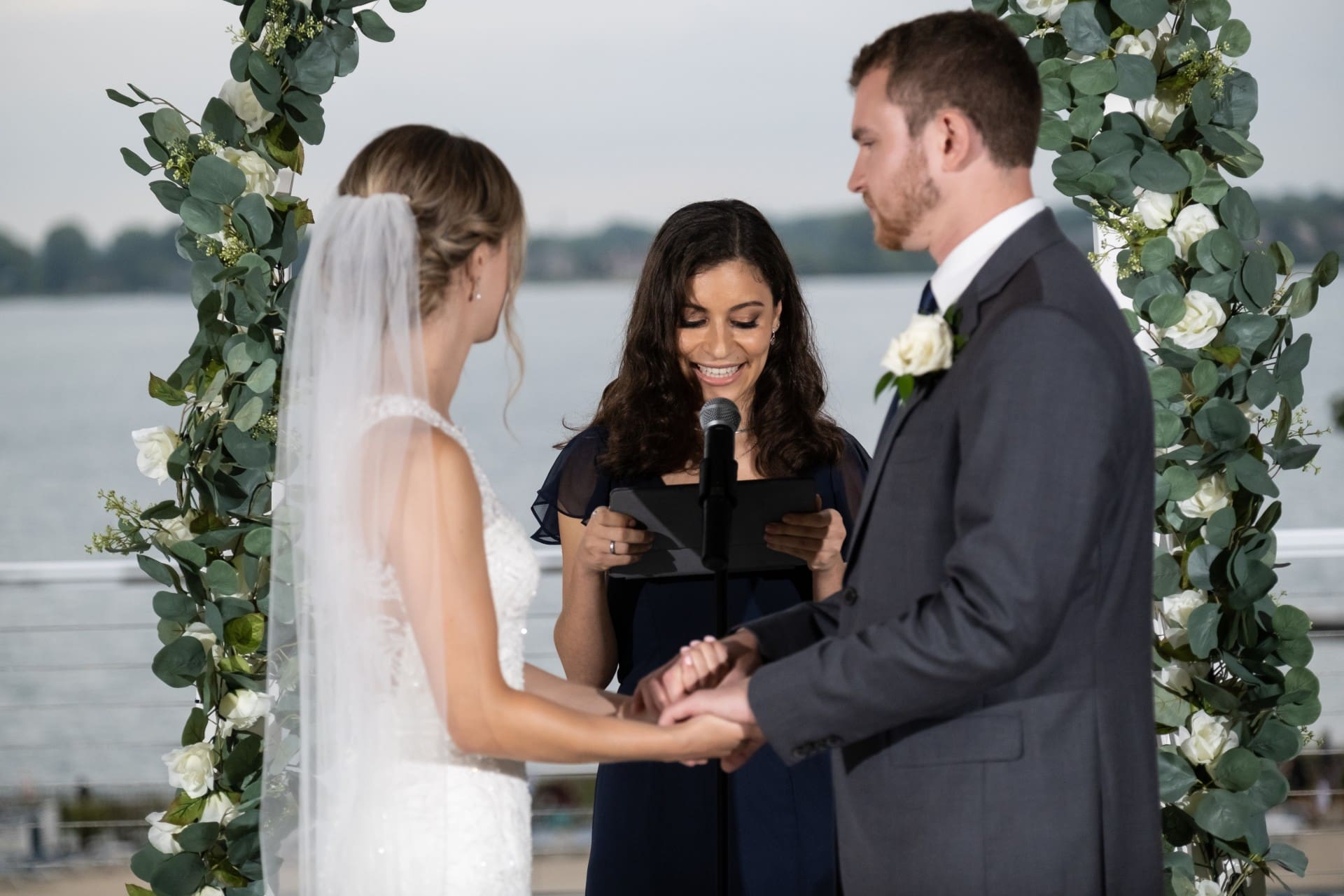 Orchard Lake wedding ceremony with bride and groom exchanging vows beside a floral arch overlooking the lake